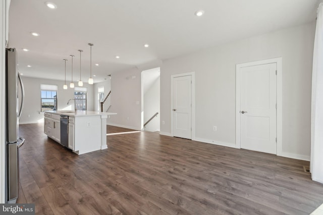 kitchen with dark hardwood / wood-style floors, decorative light fixtures, white cabinetry, stainless steel appliances, and a center island with sink