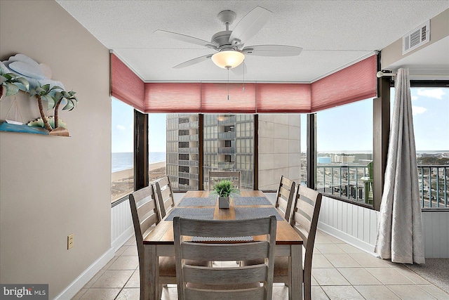 dining room featuring a water view, ceiling fan, a textured ceiling, and light tile patterned floors