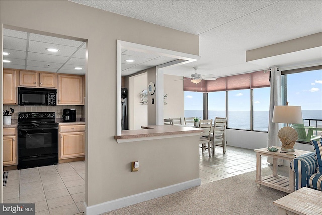 kitchen with light brown cabinetry, light tile patterned floors, black appliances, and a water view