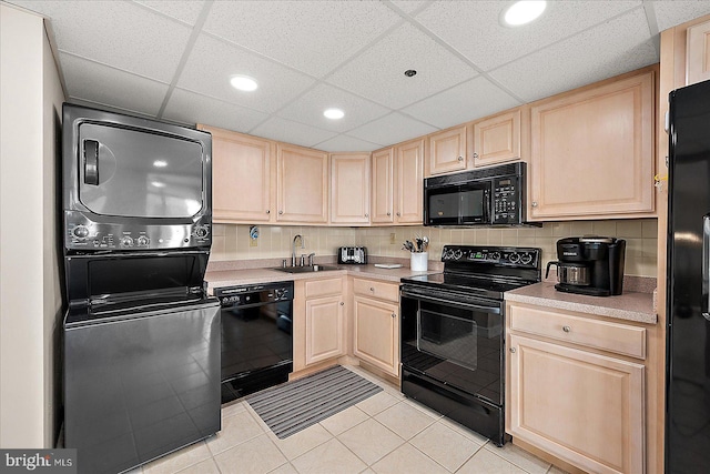 kitchen with stacked washer / drying machine, sink, light brown cabinets, and black appliances