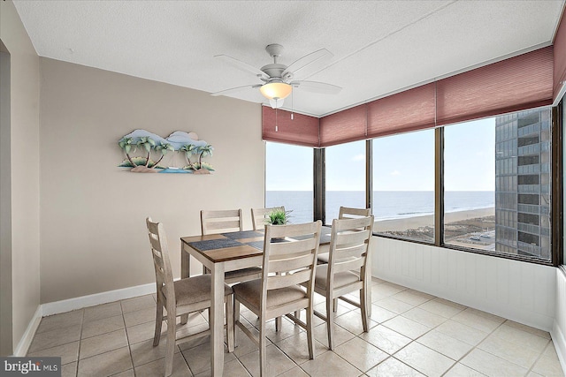 dining room featuring a water view, ceiling fan, a textured ceiling, and light tile patterned floors