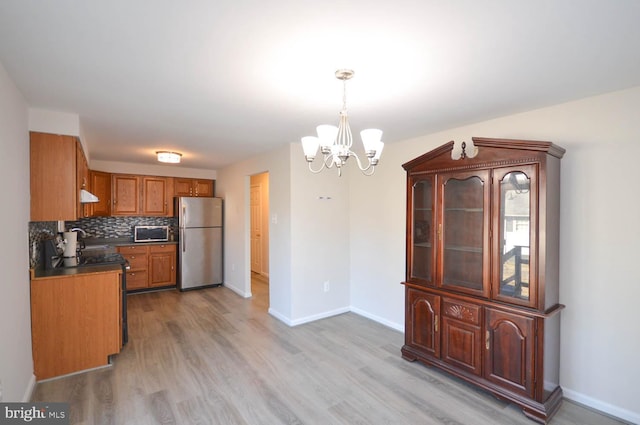 kitchen featuring tasteful backsplash, dark countertops, light wood-style flooring, appliances with stainless steel finishes, and brown cabinetry