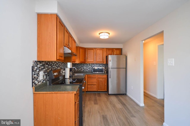 kitchen with under cabinet range hood, stainless steel appliances, a sink, backsplash, and dark countertops