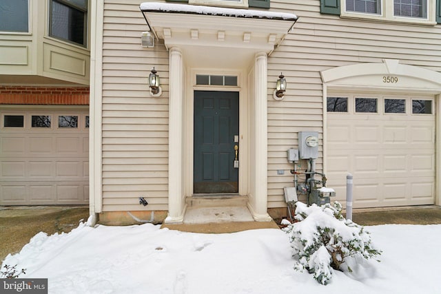 snow covered property entrance with a garage