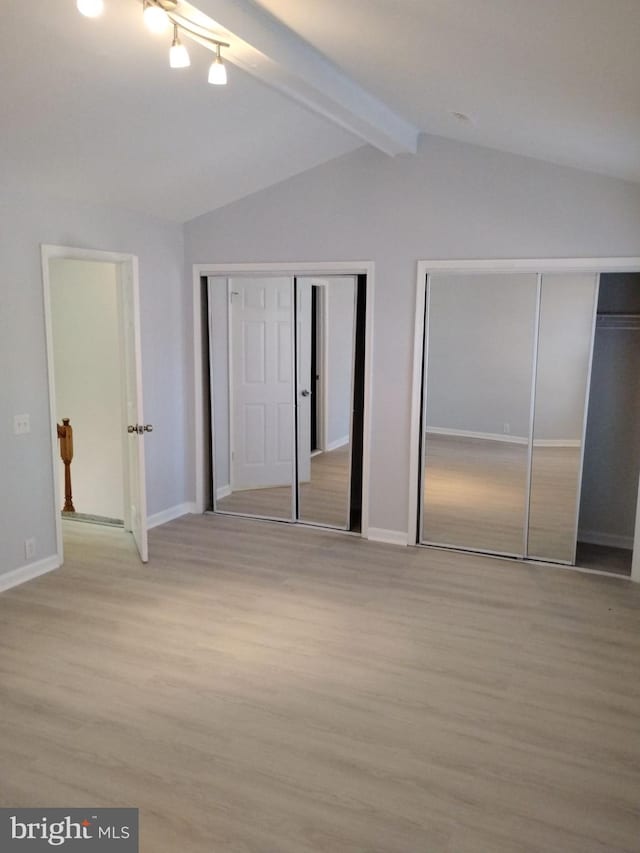 unfurnished bedroom featuring two closets, lofted ceiling with beams, and light hardwood / wood-style floors