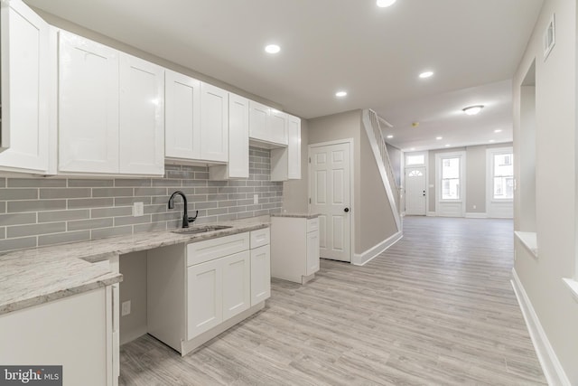 kitchen featuring light wood finished floors, tasteful backsplash, light stone countertops, white cabinetry, and a sink