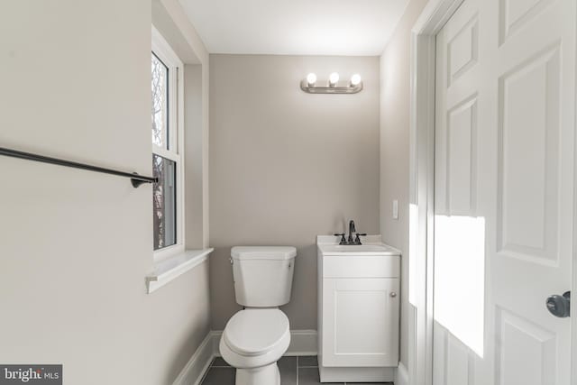 half bathroom with baseboards, vanity, toilet, and tile patterned floors