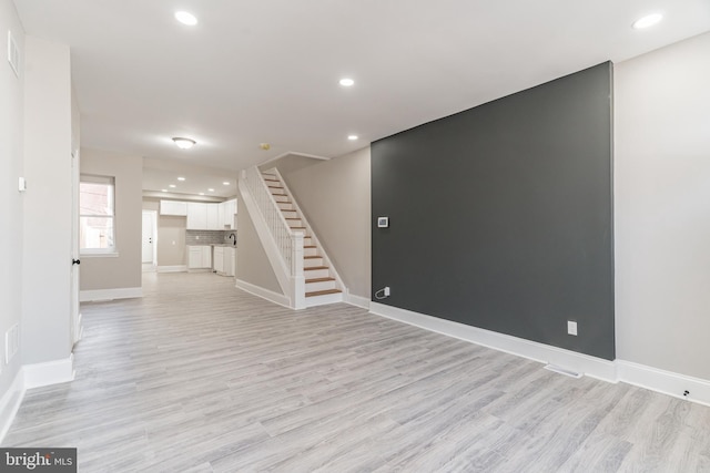 below grade area with light wood-type flooring, baseboards, and stairs