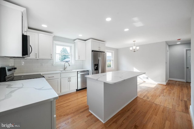 kitchen featuring white cabinetry, light stone counters, hanging light fixtures, a kitchen island, and stainless steel appliances