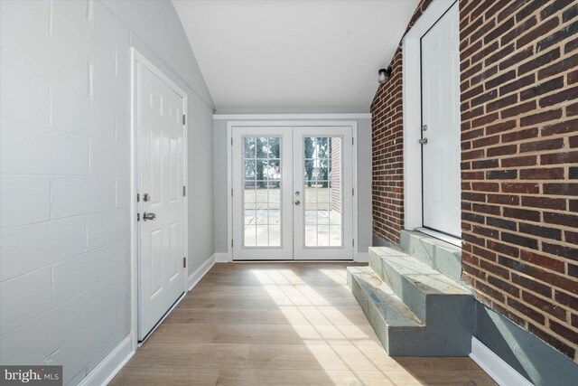 entryway with light hardwood / wood-style flooring, french doors, vaulted ceiling, and brick wall