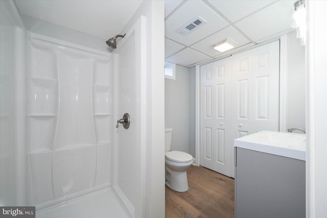 bathroom featuring hardwood / wood-style floors, a shower, vanity, toilet, and a drop ceiling