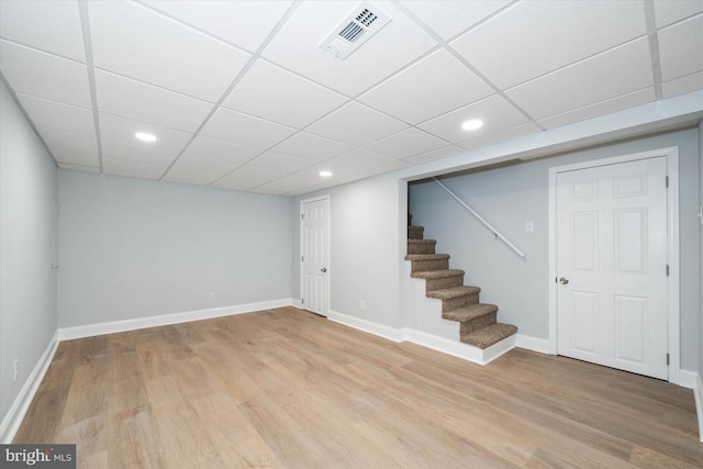 basement featuring a paneled ceiling and light hardwood / wood-style floors