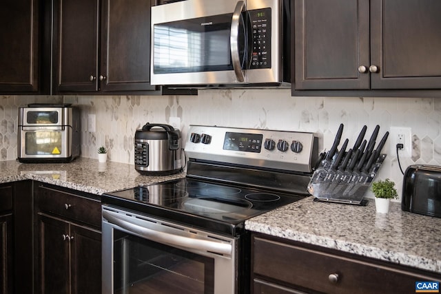 kitchen featuring stainless steel appliances, tasteful backsplash, dark brown cabinets, and light stone counters