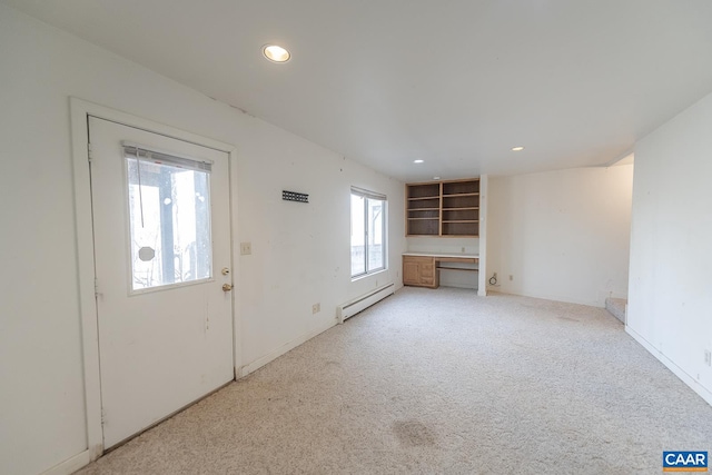 unfurnished living room featuring light carpet, built in desk, and baseboard heating