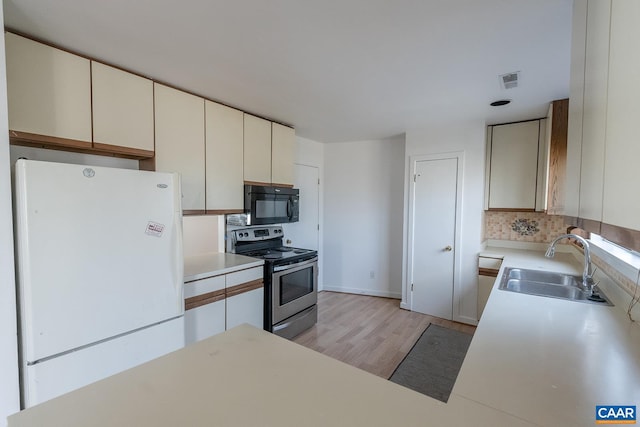 kitchen featuring sink, light hardwood / wood-style flooring, white refrigerator, cream cabinets, and stainless steel range with electric cooktop