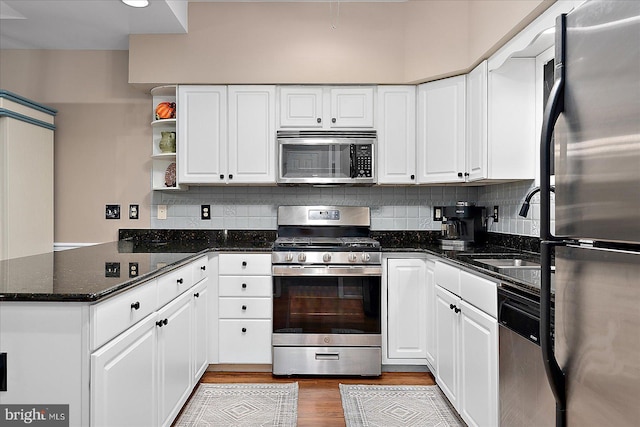 kitchen featuring white cabinetry, stainless steel appliances, kitchen peninsula, and dark stone counters