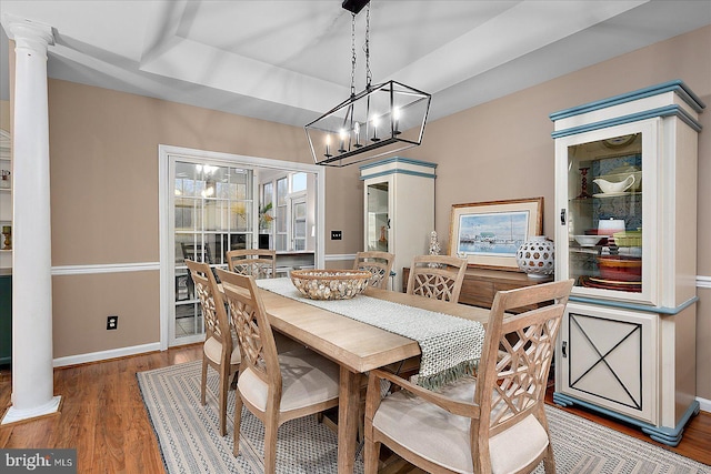 dining area featuring hardwood / wood-style flooring, a raised ceiling, and ornate columns