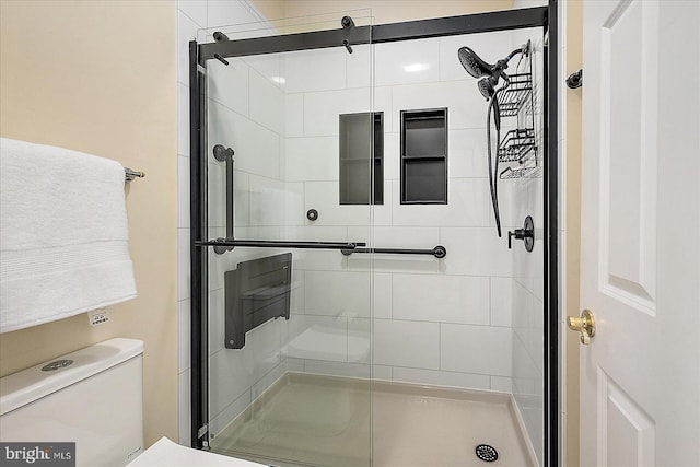 bathroom featuring a shower with door and toilet