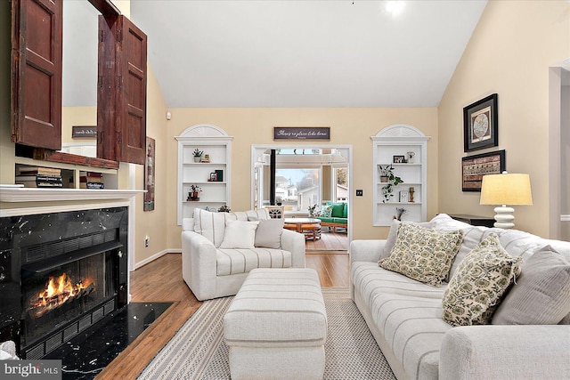 living room with lofted ceiling, built in features, a premium fireplace, and light wood-type flooring