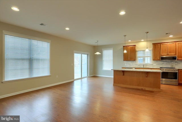 kitchen with light wood-type flooring, backsplash, a kitchen bar, and appliances with stainless steel finishes