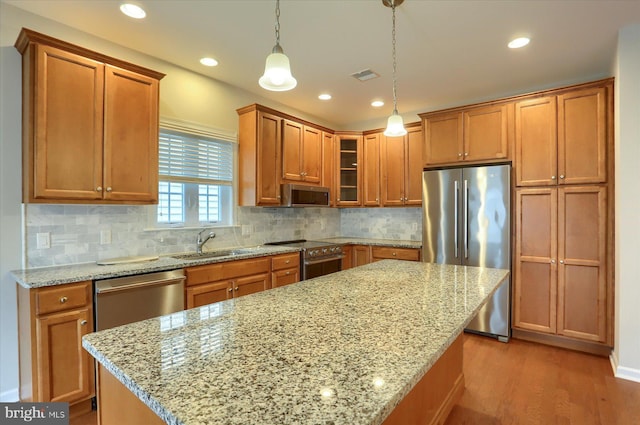 kitchen with appliances with stainless steel finishes, light stone countertops, sink, and hanging light fixtures