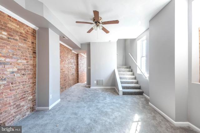 unfurnished living room featuring carpet flooring, ceiling fan, and brick wall