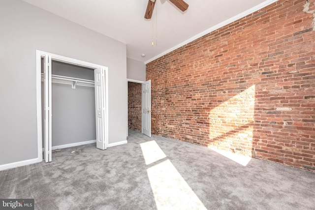 unfurnished bedroom with ornamental molding, carpet flooring, a closet, ceiling fan, and brick wall