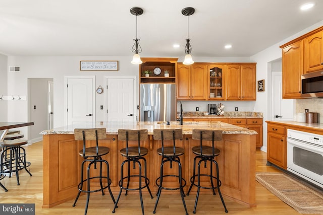 kitchen featuring light stone counters, decorative light fixtures, a kitchen breakfast bar, an island with sink, and stainless steel appliances