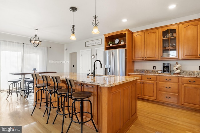 kitchen featuring sink, decorative light fixtures, a kitchen breakfast bar, stainless steel fridge, and a kitchen island with sink