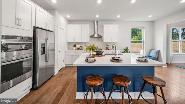 kitchen featuring appliances with stainless steel finishes, sink, a center island with sink, and wall chimney range hood