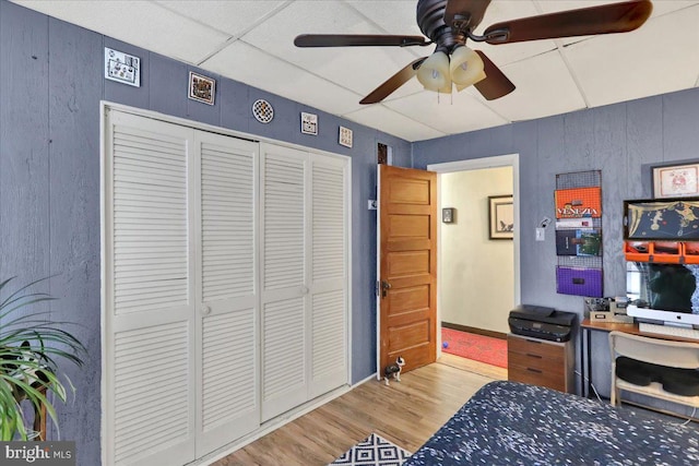 bedroom with a drop ceiling, hardwood / wood-style flooring, a closet, and ceiling fan