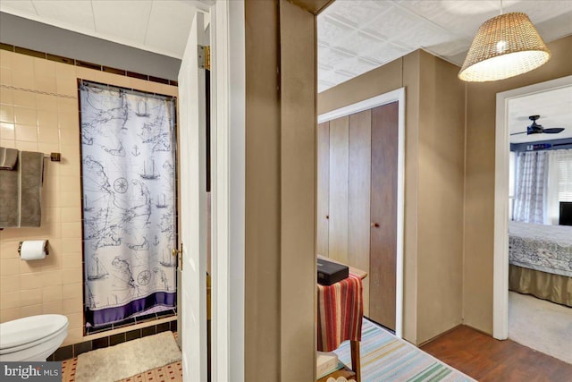 bathroom featuring wood-type flooring, tile walls, ceiling fan, and toilet