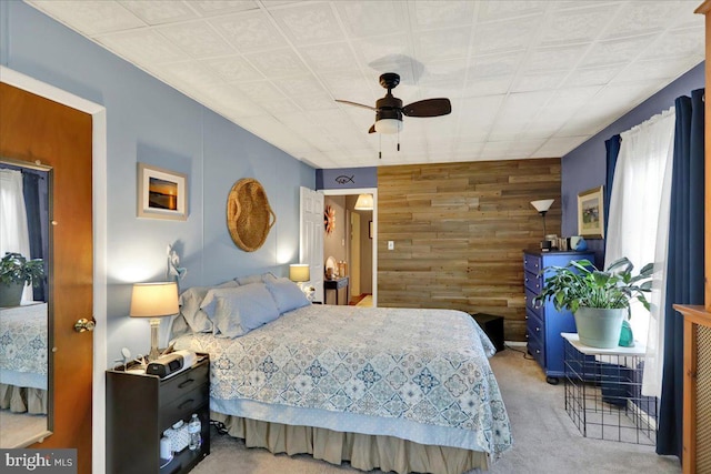 carpeted bedroom with ceiling fan and wood walls