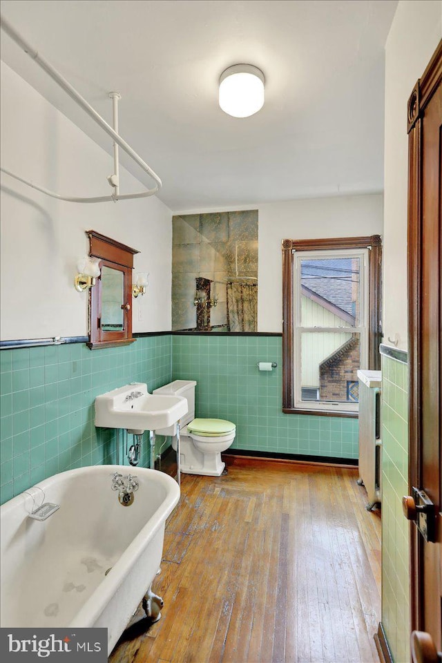 bathroom featuring hardwood / wood-style flooring, toilet, a bathing tub, and tile walls