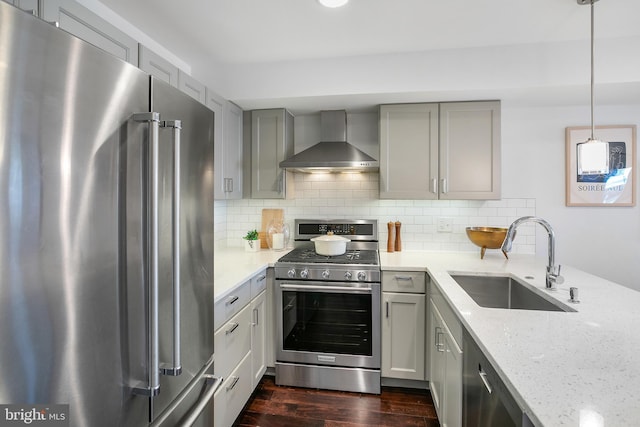 kitchen with decorative light fixtures, sink, light stone counters, stainless steel appliances, and wall chimney range hood