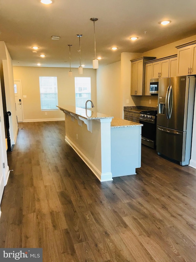 kitchen with dark wood-type flooring, a kitchen island with sink, hanging light fixtures, stainless steel appliances, and light stone counters