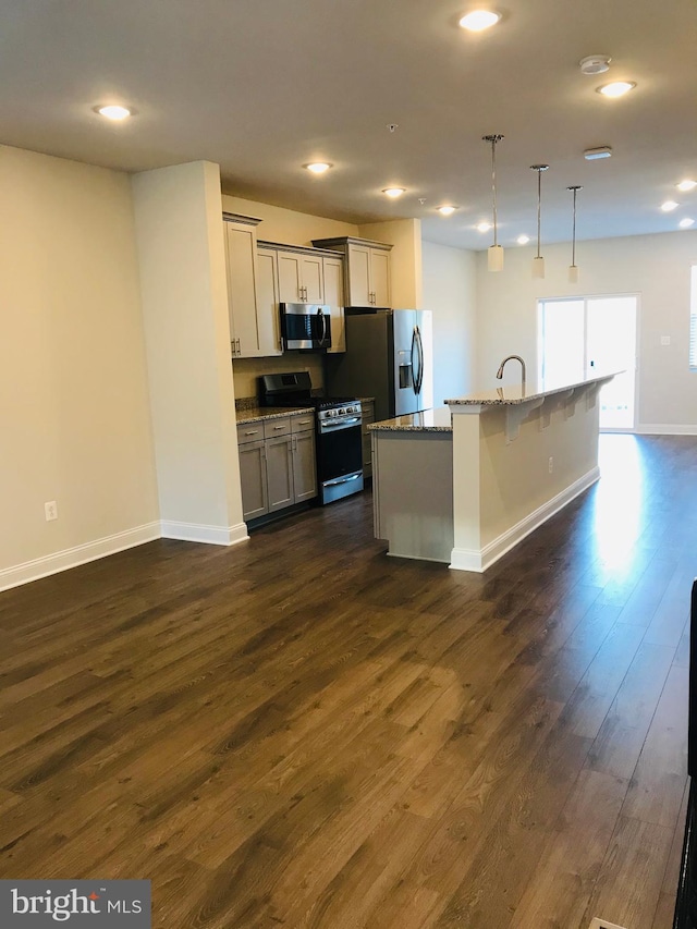 kitchen with a kitchen island with sink, hanging light fixtures, gray cabinetry, stainless steel appliances, and light stone counters