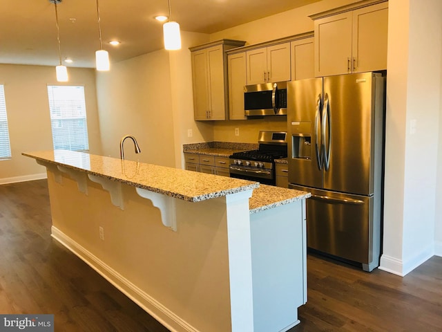 kitchen with light stone counters, appliances with stainless steel finishes, decorative light fixtures, and a center island with sink