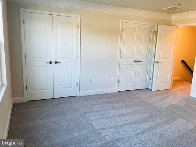 unfurnished bedroom featuring crown molding, multiple closets, and carpet flooring