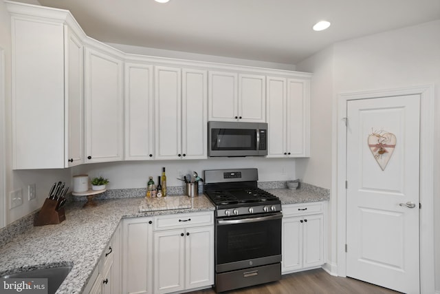 kitchen with stainless steel appliances, light stone countertops, light hardwood / wood-style floors, and white cabinets