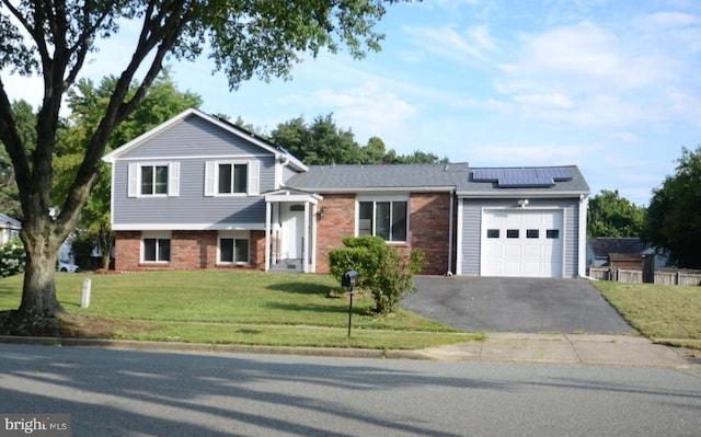 split level home featuring a front lawn, an attached garage, brick siding, and roof mounted solar panels