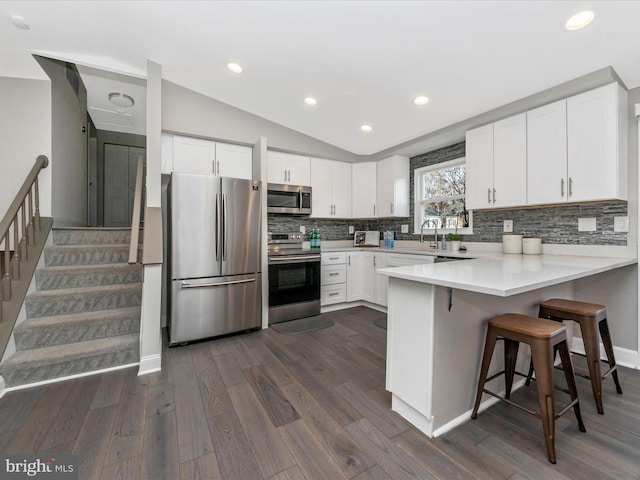 kitchen with lofted ceiling, decorative backsplash, appliances with stainless steel finishes, white cabinetry, and a peninsula