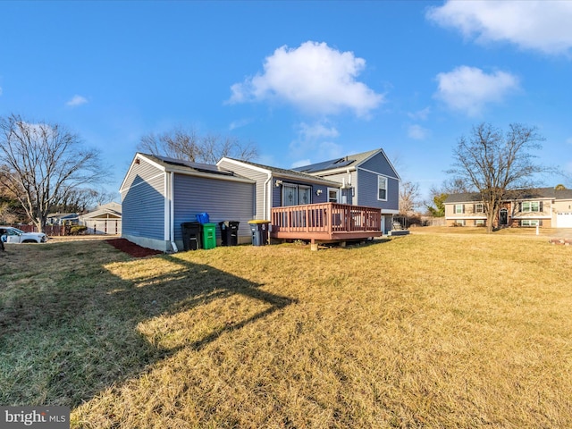 rear view of property featuring roof mounted solar panels, a lawn, and a wooden deck