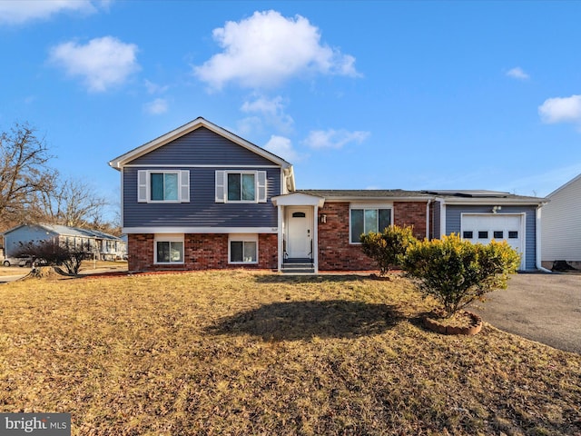 tri-level home featuring a garage, a front lawn, aphalt driveway, and brick siding