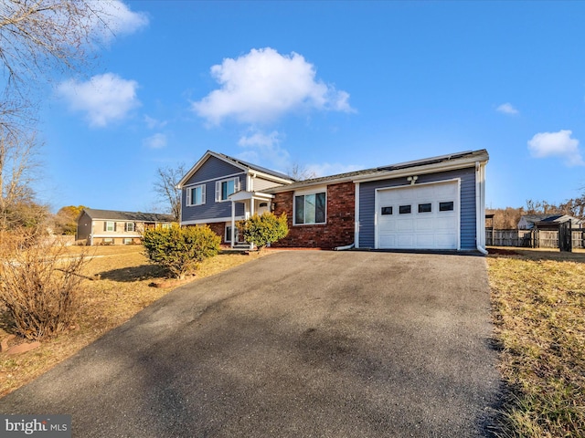 tri-level home with a garage, driveway, roof mounted solar panels, and brick siding