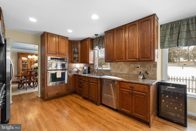 kitchen with pendant lighting, sink, appliances with stainless steel finishes, light stone countertops, and beverage cooler