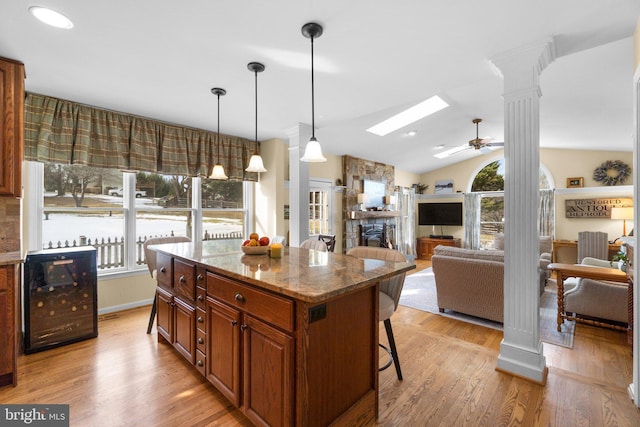 kitchen with a breakfast bar, light stone counters, a center island, pendant lighting, and vaulted ceiling with skylight