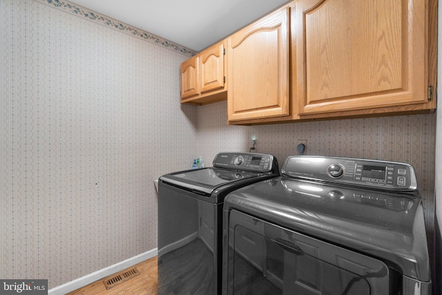 clothes washing area with cabinets, light hardwood / wood-style floors, and washer and dryer