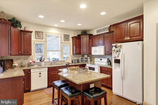 kitchen with sink, white appliances, a breakfast bar, a center island, and light hardwood / wood-style floors