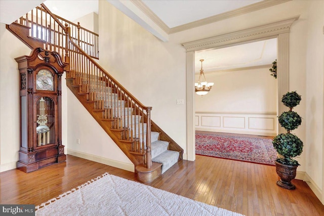 stairs featuring hardwood / wood-style flooring, ornamental molding, and a notable chandelier